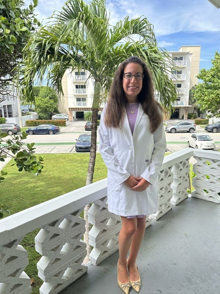 Dr. Lisa Fuchs seated, wearing a white coat with embroidered name.